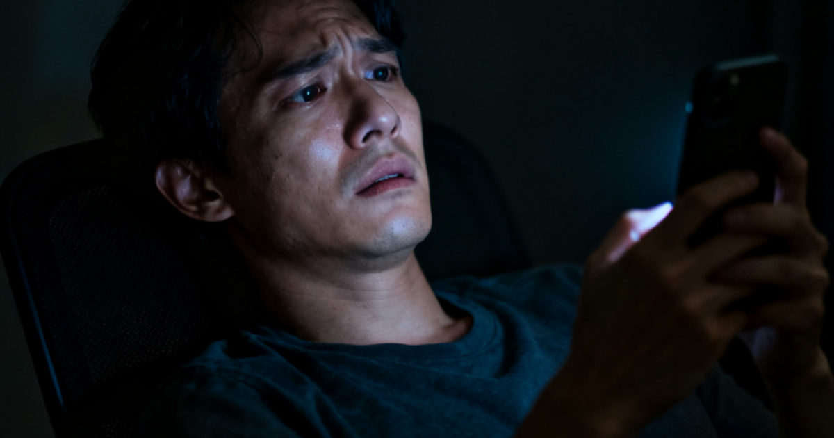 Ilustrasi seseorang yang terlihat cemas dan lelah saat menatap layar ponsel di dalam ruangan yang gelap.